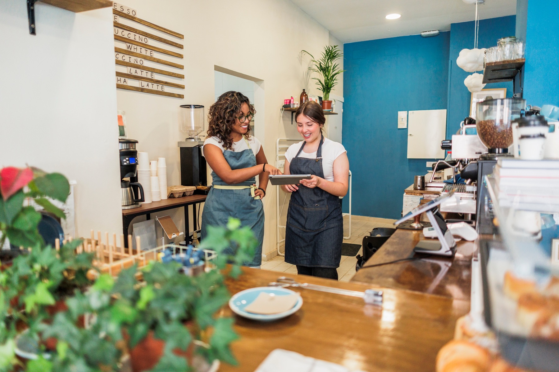 Two café owners checking something together on a tablet behind the counter