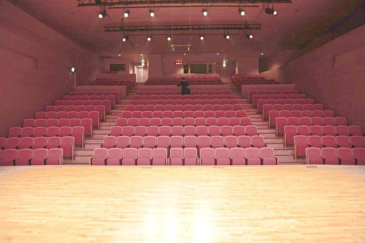 Rows of empty red seats in a small theatre, seen from the stage